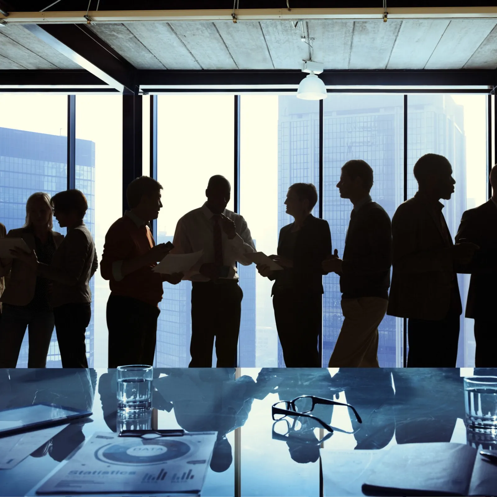Silhuetas de executivos conversando de pé diante da janela de uma sala de reunião